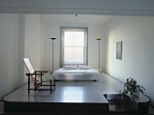 Rietveld-Stuhl und ein Doppelbett mit zwei Stehlampen auf einem Podest im Schlafzimmer