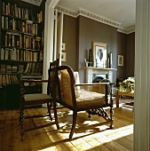 Traditionelles Wohnzimmer mit Dielenboden und antiken Sitzmöbeln aus Holz vor Bücherwand