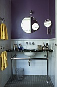 Runde Spiegel an fliederfarbener Wand über Marmorwaschtisch auf Metallgestell in kleinem Bad