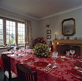 Festlich gedeckte Tafel mit roter Tischdecke, roten Tellern und Kristallgläsern in traditionellem Esszimmer