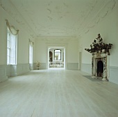 Grosser, leerer Saal im Georgian Stil mit weiss lasierten Holzdielen, reich verzierter Stuckdecke und Kamin mit Marmorsäulen