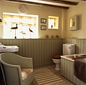 Englischer Sessel in Landhaus-Badezimmer mit hellgrüner Wandverkleidung und Stranddeko