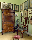 Antiker Stuhl, Kommode und eingerahmte Bilder mit Vogelmotiven in einer lindgrünen Halle