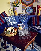 Ein rustikaler Holztisch mit Gläsern vor der blauen Sofa mit bunten Kissen