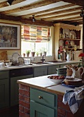 Eine ländliche Küche mit Kücheninsel und buntem Raffrollo über dem Spülbecken