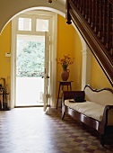 Ein weisses Sofa aus dem 19. Jh. in einer typisch ländlichen Eingangshalle mit braunen und cremefarbenen Fliesen und offener Haustür