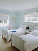 weiße Jalousien am Fenster im türkis pastellfarbenen Schlafzimmer mit weißen Leinentüchern auf weißen Einzelbetten aus Holz
