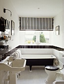 Schwarz-weiß gestreifte Jalousien sind überhalb einer freistehenden schwarzen Badewanne angebracht worden und werden in der schwarzen Kacheln-Leiste erwidert