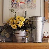 Eine Nahaufnahme von einem Blumentopf mit gelben Chrysanthemen, der neben einer Metall-Vase steht