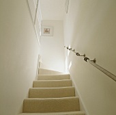 Eine Treppe mit einem hellen Teppich und einen Handlauf aus Metall, die zu dem oberen Geschoß führt