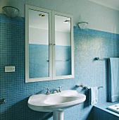Ein Spiegelschrank, unter dem ein weißes Waschbecken steht, wurde in der einen blauen Mosaik-Wand des modernen Badezimmers eingebracht
