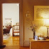 Brennende Lampe mit altmodischem Messingfuss auf Kieferntruhe neben der offenen Tür zum traditionellen Schlafzimmer mit Holzboden