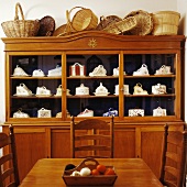 Körbesammlung auf schlichter, alter Holzvitrine mit Sammlung antiker Käseglocken hinter Essplatz in gleicher Holzfarbe