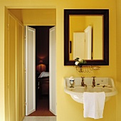 Spiegel mit dunklem Holzrahmen über Waschbecken mit Messingarmatur in gelbem Bad ensuite