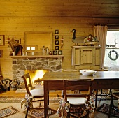 Alter hölzerner Esstisch vor Kamin mit Polygonalplatten-Verkleidung und Holzverschalung in rustikalem Esszimmer
