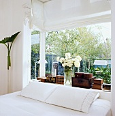 Kopfende eines Doppelbettes vor Blumenfenster mit verschiedenen Holzkistchen und Blumenstrauss