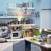 weiße Küchenwand mit Borden voller Geschirr, Bechern an Haken und Beleuchtung durch Retro-Lampe