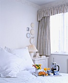 Frühstückstablett mit Kaffeebereiter auf Bett in weißem Schlafzimmer mit zarter Schablonenbordüre