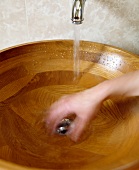 Durch Bewegung unscharfe Ansicht einer Hand unter fliessendem Wasser in hölzernem, runden Waschbecken