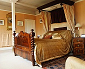 Schlafzimmer mit golden gemusterter Bettdecke auf gewaltigem Mahagoni-Himmelbett vor pfirsichfarbener Wand