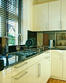 Schwarze Fensterjalousie über Spülbecken in moderner Küche mit elfenbeinfarbenen Einbauschränken und schwarzer Granit-Arbeitsplatte