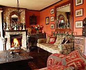 Rustikales Wohnzimmer mit antikem Metallsofa und weiteren alten Möbeln um einen unverputzten Kamin mit loderndem Feuer