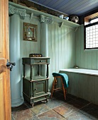 Kleine, antike Kommode zwischen klassischen Säulen in holzverschaltem Badezimmer in Hellgrün und Blautönen