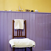 weiße Handtücher auf einem Holzstuhl vor fliederfarbener Wandtäfelung