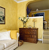 Ein gelbes Wohnzimmer mit einem weißen Sofa und einer Kommode