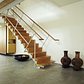 Große Töpfe neben einer Treppe aus Holz und Metall in einem weißen Saal mit Steinboden
