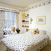 Kinderzimmer mit blau und gelb gemusterter Bettwäsche und gleichgemusterten Vorhängen, dazu einen Tapetenrand mit Entenmotiv