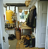 Bäuerliche Diele mit altem Boiler, Steinfliesen, Reitstiefeln, Jacken, Hüte, Körben und Hund