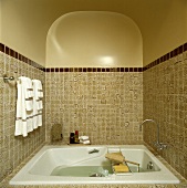 Traditionelles Badezimmer mit beigen Kacheln, einer kleinen Badewanne in einer Nische und Handtücher auf einer Handtuchschiene
