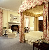 Herrschaftliches, pastellgelbes Schlafzimmer mit Himmelbett mit Toile-de-Jouy Vorhänge, cremefarbener Bettdecke und grauem Teppichboden