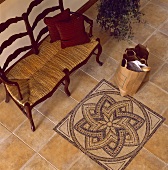 Holzbank mit Strohsitz auf einem Fliesenboden mit kunstvollen Mosaik-Mustern