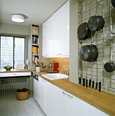 weiße Küche mit Holzarbeitsfläche und Wandgitter für die Pfannen und Töpfen