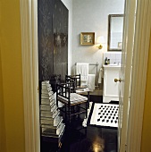 Blick in ein schwarz-weisses Badezimmer mit gestapelten Aluminiumdosen neben einem antiken Stuhl