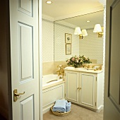 Blick in ein cremefarbenes Badezimmer mit einer Spiegelwand und Wandlampen