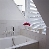 Weiß gefliestes Badezimmer mit Fenster und Jalousien in einem Dachgeschoss