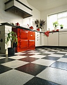 Schwarz-weiße Keramikfliesen, weiße Schränke und roter Ofen in einer Küche