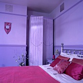 Pinkfarbene Seidenkissen und rosa Bettdecke auf dem Bett in einem lila Schlafzimmer mit lila Kleiderschrank