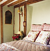 Doppelbett mit gemusterter Tagesdecke und Kissen in einem ländlichen Schlafzimmer mit Holzbalkendecke