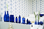 Badezimmer mit blau-weisser Tapete und blauen Flaschen auf dem Regal über der Badewanne