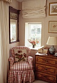 Rot-weiß karierter Sessel neben antiker Kommode mit Schubladen vor kleinem Fenster in Zimmerecke