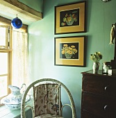 Bilder an Wand in türkisfarbener Zimmerecke und Wasserkrug auf Fensterbank
