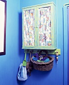 Grünes Wandschränkchen mit Vorhängen hinter verglasten Türen an blauer Wand in Zimmerecke