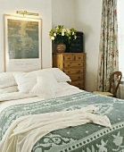 Schlafzimmer mit weißer Bettwäsche und gemusterter grüner Tagesdecke auf Doppelbett darüber Bild mit Beleuchtung