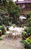 Schmiedeeiserne Stühle und Tisch in Weiß mit Blumen in Töpfen auf Terrasse im Stadtgarten eines englischen Wohnhauses