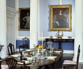 Gedeckter Mahagonitisch in einem pastellblauen Esszimmer mit Säulen und Portraitmalerei an der Wand