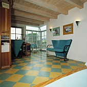Türkis Sofa in einem Wohnzimmer mit Holzdecke und gelb-türkis Schachbrettmuster-Boden